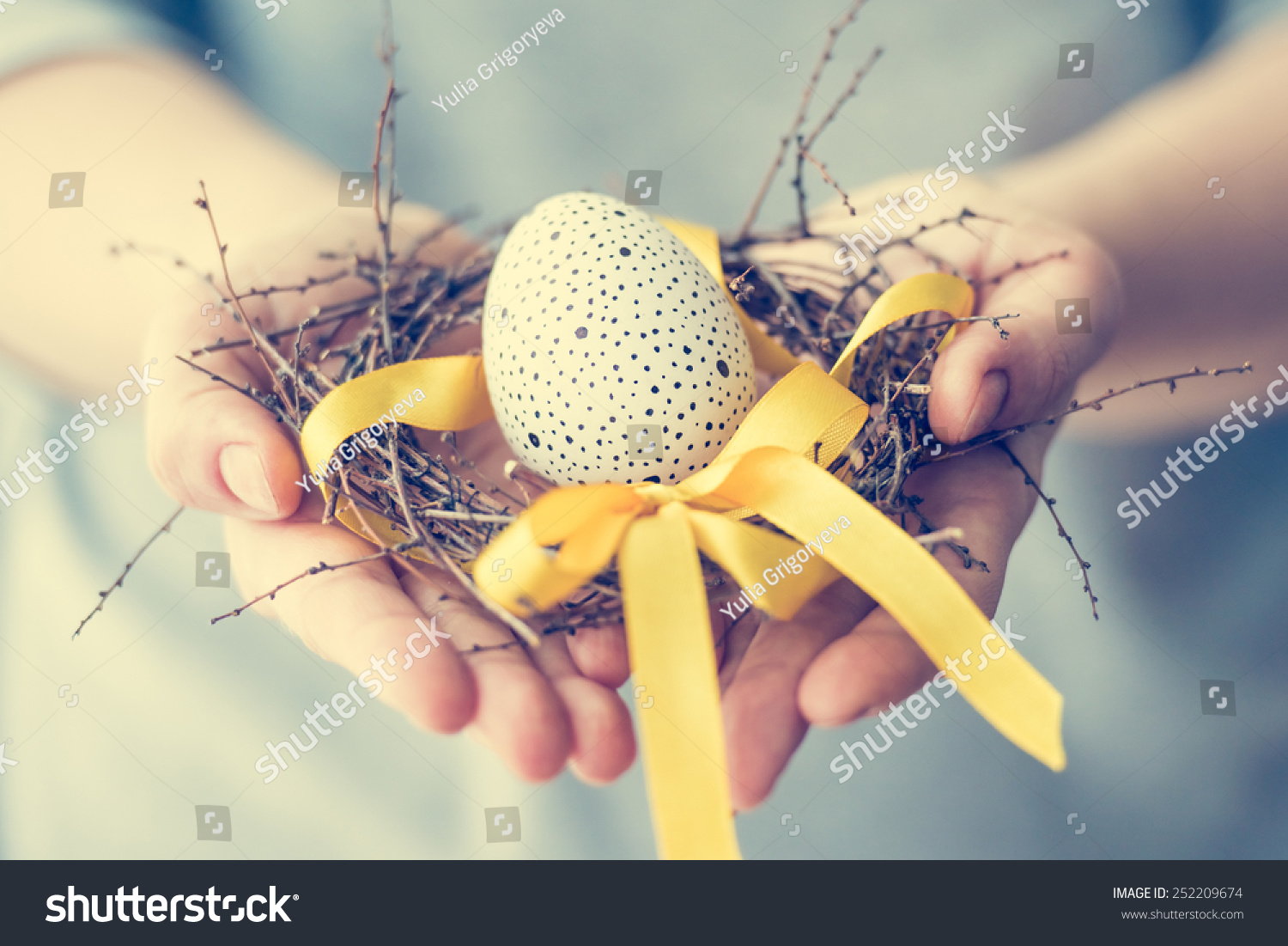 stock-photo-hands-holding-modern-painted-easter-egg-in-a-small-nest-toned-picture-252209674.jpg