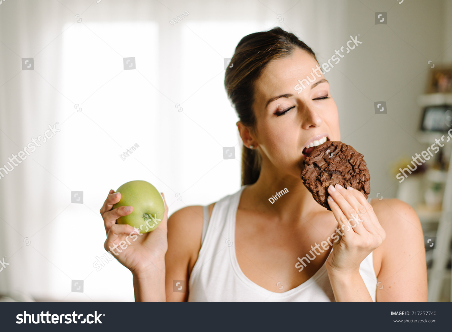 to-hungry-woman-on-a-diet-chooses-to-eat-a-chocolate-cookie-instead-of-a-healthy-apple-717257740.jpg